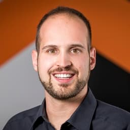 Ein Mann mit kurzen Haaren und einem Bart. Er trägt ein dunkelblaues Hemd.