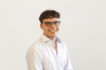 Ein Mann mit kurzen, lockigen Haaren. Er trägt eine Brille und ein Hemd.