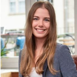 Eine Frau mit langen, dunkelblonden Haaren. Sie trägt einen gestreiften Blazer im Business Casual-Style.