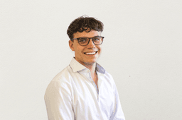 Ein Mann mit kurzen, lockigen Haaren. Er trägt eine Brille und ein Hemd.